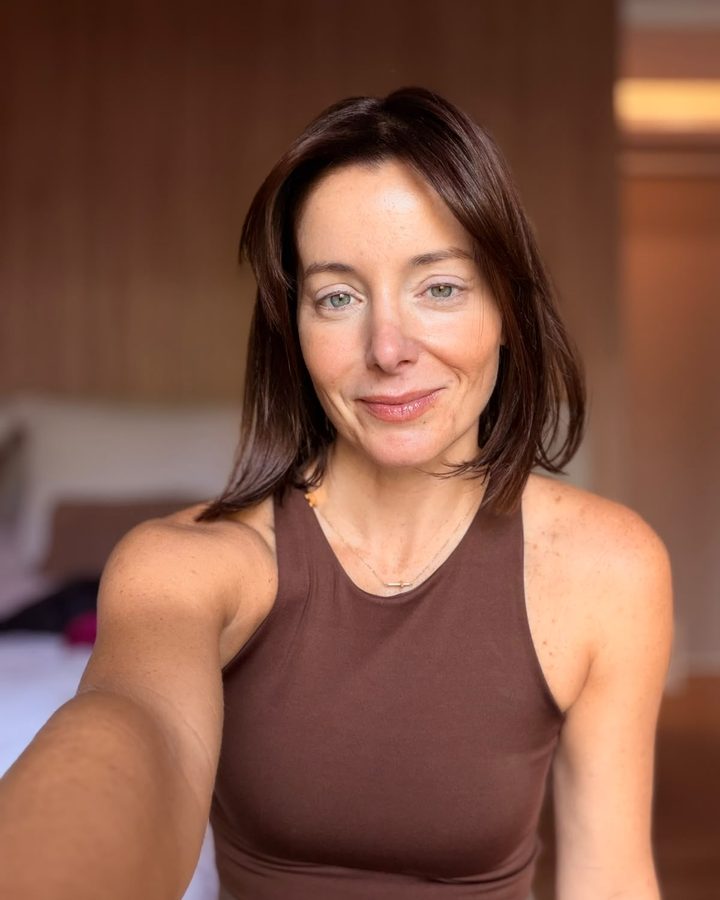 Mili Pavan sorrindo, de blusa marrom, em um ambiente com luz quente